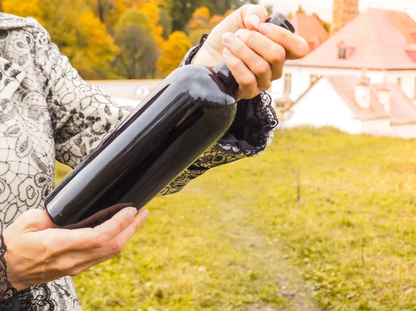 Bottiglia di vino rosso in mani femminili sullo sfondo di un antico castello . — Foto Stock