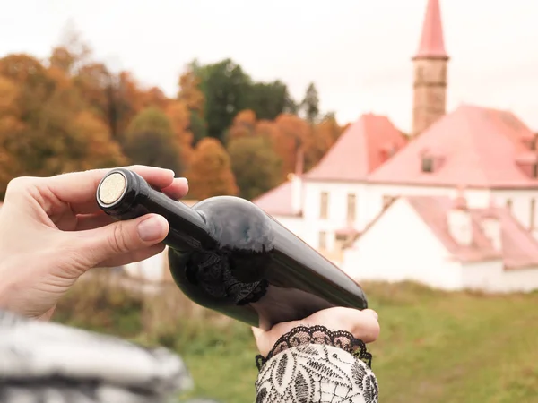 Bottiglia di vino rosso in mani femminili sullo sfondo di un antico castello . — Foto Stock