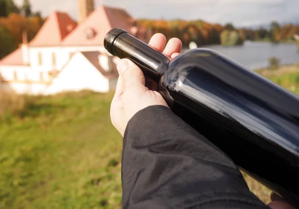 Bottiglia di vino rosso nelle mani di un uomo in mantello nero . — Foto Stock