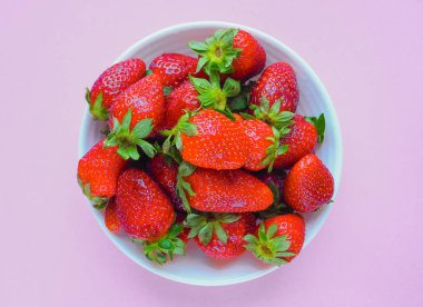 Pembe bir arka plan üzerinde beyaz tabak içinde taze çilek. Üstten Görünüm.