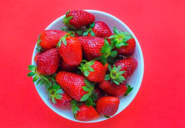 Taze çilek kırmızı zemin üzerine beyaz tabak içinde. Üstten Görünüm.