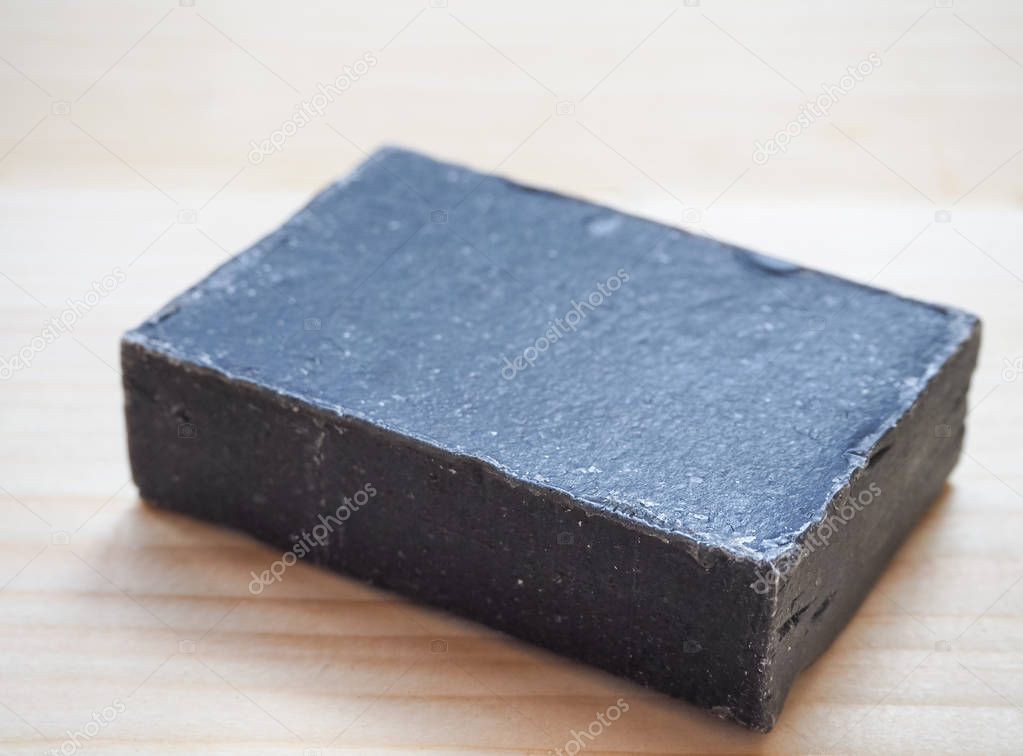 Block of natural black carbon soap on wooden background.