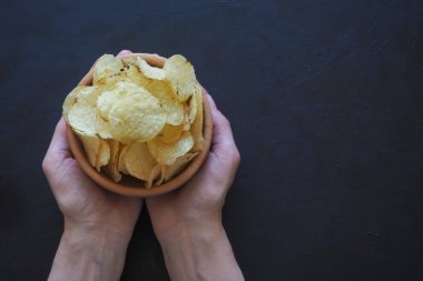 Lezzetli patates cipsi karanlık bir arka plan üzerinde tutan kadınların elleri.