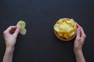 Lezzetli patates cipsi karanlık bir arka plan üzerinde tutan kadınların elleri.