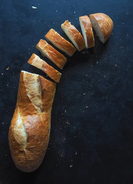 Fresh, delicious baguette on the black table. Cut baguette. — Stock Photo, Image