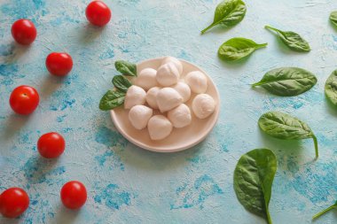 İtalyan mozzarella peyniri, domates, ıspanak yaprakları üzerinde mavi bir tablo.