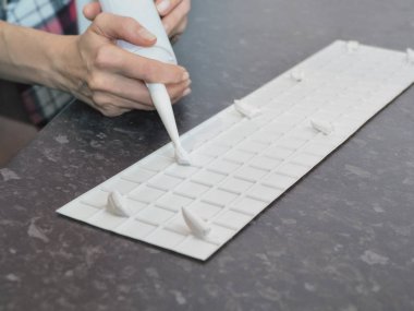 Duvara plastik beyaz tahta paneli yapıştırmaya yakın çekim. Adam el ele tutuşup yapıştırıcı kullanıyor, silikon tüp.