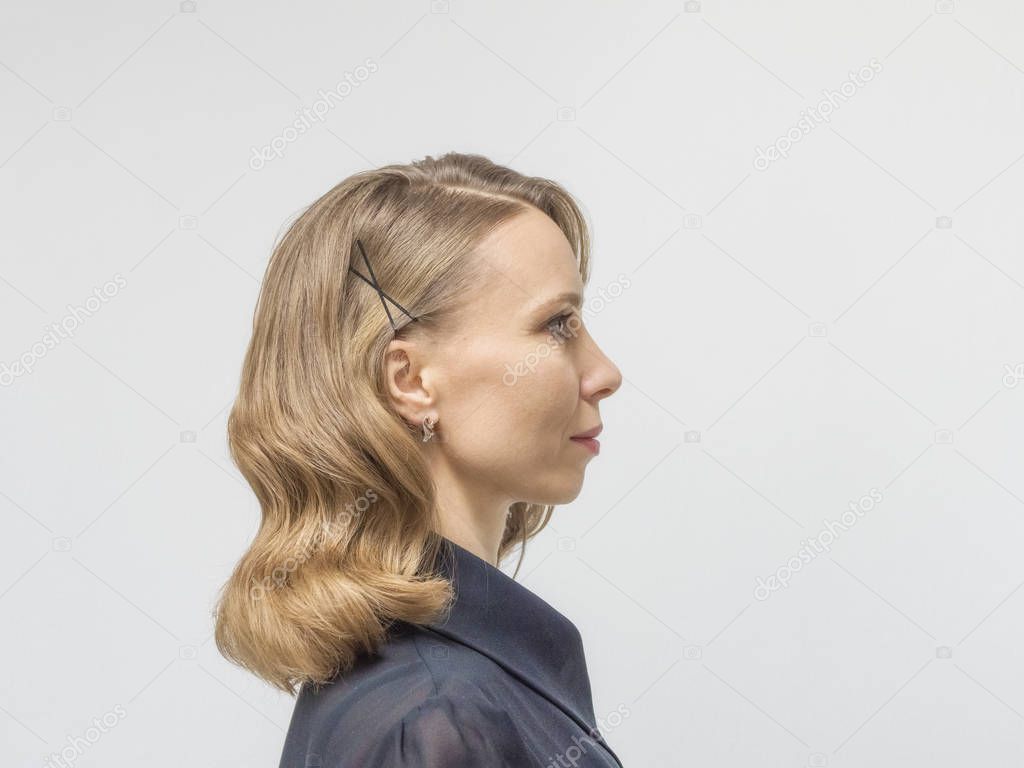 Woman with long blonde hair and elegant hairstyle in retro style of wavy hair in a beauty salon. Side view