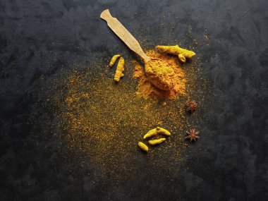 Siyah zemin üzerinde zerdeçal tozu ve kök zerdeçal