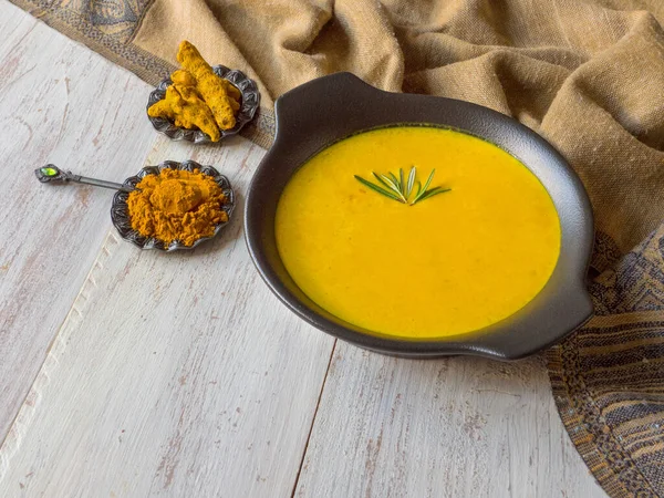 Healthy curcuma cream soup on white wooden background