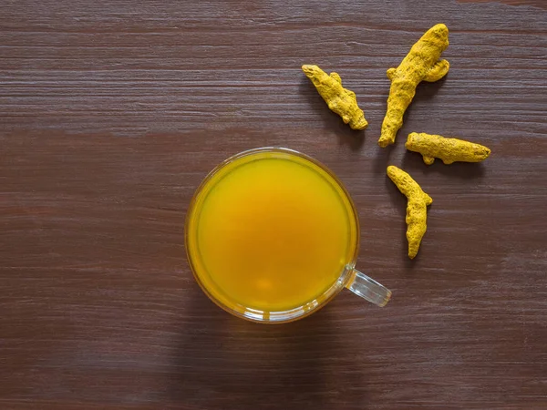 Herbal tea with turmeric powder and turmeric roots on a brown table
