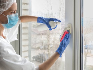 Coronavirus dezenfeksiyonu. Pencerelerde dezenfeksiyon yapan insanlar. Lastik eldivenli doktor pencereleri dezenfektan ve süngerle dezenfekte eder.