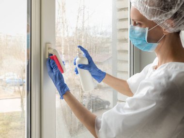 Coronavirus dezenfeksiyonu. Pencerelerde dezenfeksiyon yapan insanlar. Lastik eldivenli doktor pencereleri dezenfektan ve süngerle dezenfekte eder.
