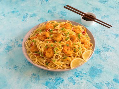 Mavi bir masada sebzeli karides Schezwan Eriştesi