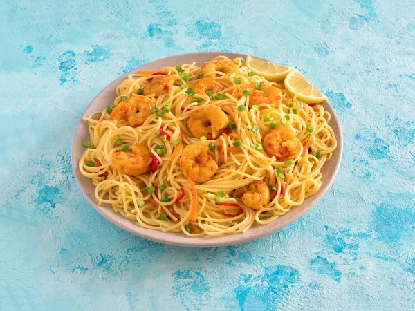 Fideos Schezwan de gambas con verduras en un plato sobre una mesa azul —  Fotos de Stock