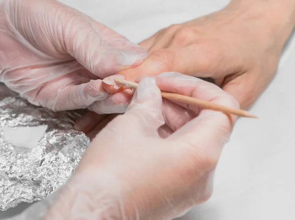 Manicurista rimuove il cappotto di base dal chiodo con un bastone arancione durante la procedura di manicure presso la Spa . — Foto Stock