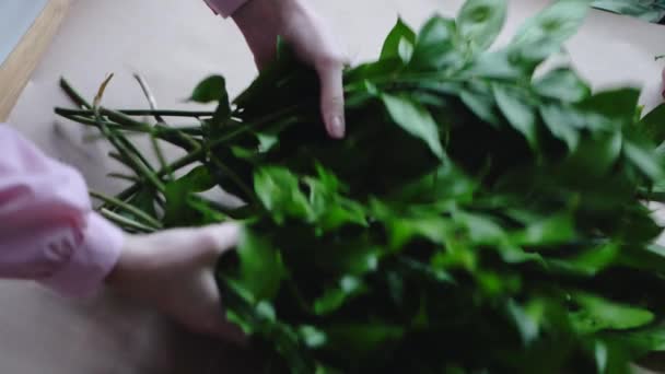 Florista coloca verdes em uma folha vazia de papel kraft para o arranjo de um buquê — Vídeo de Stock