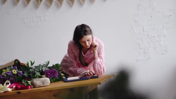 Florista menina escreve notas em um caderno e conta com a calculadora atrás do balcão — Vídeo de Stock