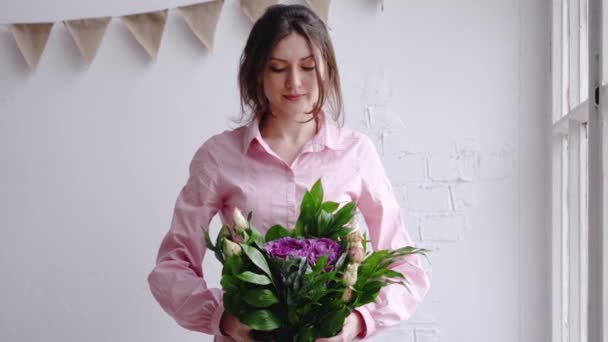 Florista chica mira a la cámara y muestra el ramo. Retrato en una florería — Vídeos de Stock