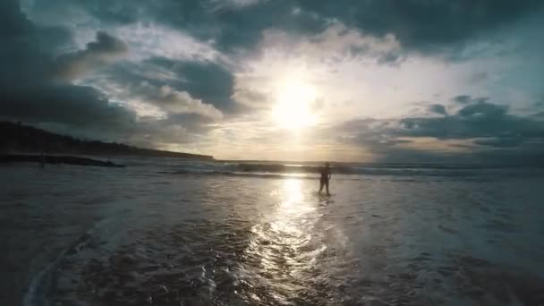 Silhuetten av en man som kör ur havet i solnedgången — Stockvideo