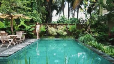 Genç bir kız bir mayo ormanın içinde belgili tanımlık havuz kenarı boyunca yol gösterir. Bali