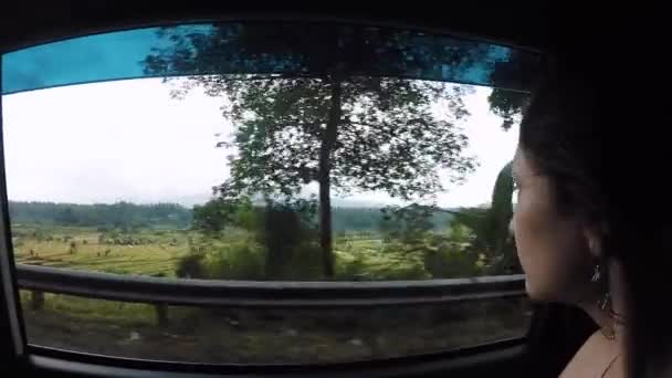 Ragazza cavalca in auto e guarda fuori dalla finestra terrazze di riso e vulcano Agung tra le nuvole — Video Stock