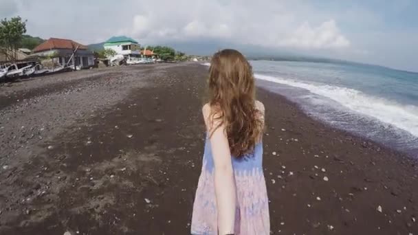 Första person vy: glada leende flicka håller hand och körs på en svart strand från vulkanisk sand i Bali långsam rörelse — Stockvideo