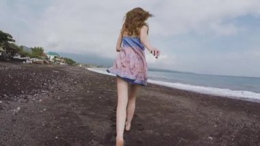 Bir genç kız güzel bir elbise içinde çalışır ve siyah beach çevresinde gelen volkanik kum Bali'ye görünüyor.