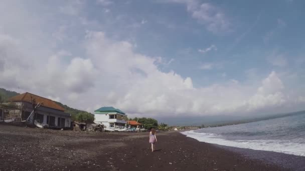 Дівчина вдалині гуляє босоніж на красивому чорному пляжі вулканічного піску — стокове відео