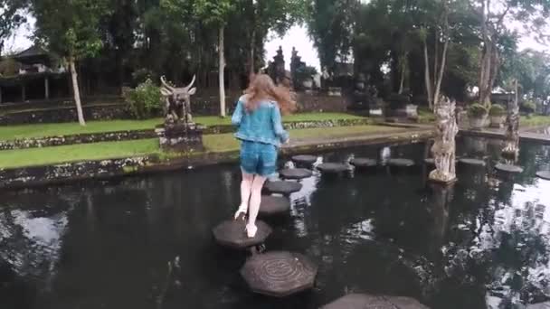 Uma menina turística corre ao longo de azulejos em uma lagoa em um belo templo balinês Tirta Gangga, câmera lenta — Vídeo de Stock