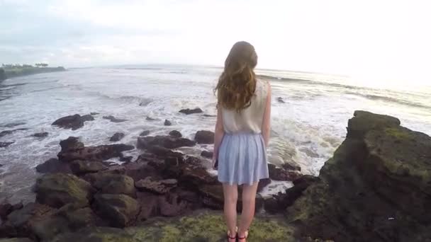 Fraai gevormde en hoog meisje staat op een rots aan de kust van de Oceaan op het eiland Bali — Stockvideo