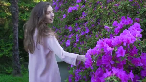 Chica camina sobre un gran macizo de flores brillantes y mira a la cámara — Vídeo de stock