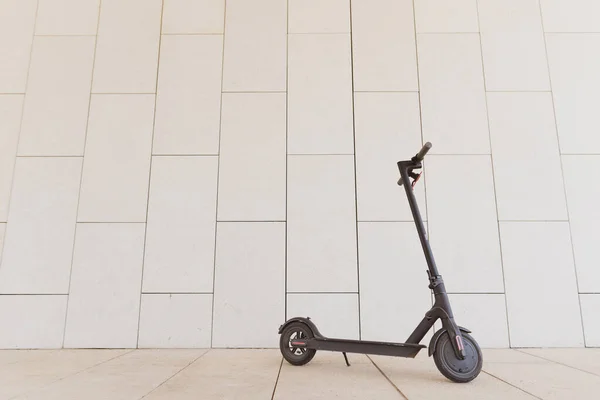 Negro elegante scooter eléctrico de pie contra una pared de hormigón en un día soleado. Transporte respetuoso con el medio ambiente —  Fotos de Stock