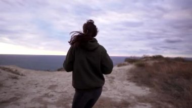 Mutlu kadın koşuyor. Neşeli bir sporcu kız sevinir ve denizin üzerinde bir kayanın üzerinde eğlenir. Açık hava fitness