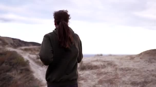 Chica corredor está entrenando en un alto acantilado sobre el mar. Correr por la mañana en la naturaleza junto al océano. Ejercicio cardiovascular en tiro de seguimiento de sudadera — Vídeos de Stock