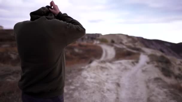 Entrenamiento en mal tiempo. Una joven con una sudadera camina en una montaña situada sobre el mar. Chica en ropa deportiva en la naturaleza — Vídeos de Stock