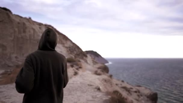 Correr en un acantilado junto al océano. Chica atleta en una sudadera caliente se dedica al ejercicio cardiovascular en la naturaleza. Fitness al atardecer, estilo de vida saludable — Vídeos de Stock