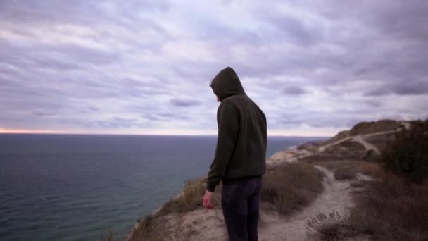 Healthy lifestyle. A beautiful caucasian woman in a sweatshirt and leggings stands on the edge of a cliff after finishing a workout. The concept of freedom and tranquility in nature — Stock Video