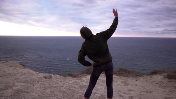 Stretching övningar i naturen, en ung kvinna tränar över havet på kvällen eller på morgonen. Idrottskropp, energi- och koncentrationskoncept utomhus — Stockvideo