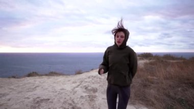 Pozitif atlet dışarıda antrenman yaparken eğleniyor ve aylaklık ediyor. Spor kazaklı ince bir kadın doğada dans ediyor ve gülümsüyor.