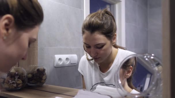 Una joven se lava la cara con agua fría antes de maquillarse en el baño. Limpieza facial y cuidado de la piel. Reflexiones en varios espejos — Vídeo de stock