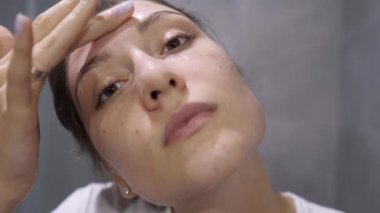 Yıkanmak için köpüklü yüz bakımı, kameraya bakan güzel bir kız. Banyodaki kadın portresi. Tazelik, kozmetik ve sağlık
