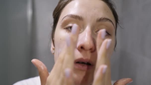 Gesichtswäsche - ein Mädchen trägt Gesichtsschaum auf ihre Haut auf, während es in die Kamera blickt. Naturkosmetik natürlichen Ursprungs — Stockvideo