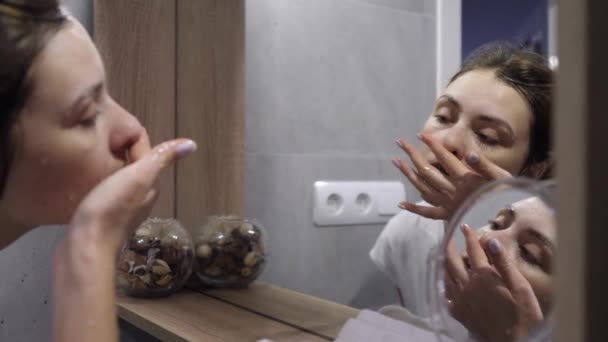 Кавказька жінка перед дзеркалом у ванній кімнаті. Умивання обличчя, догляд за шкірою, спритність. — стокове відео