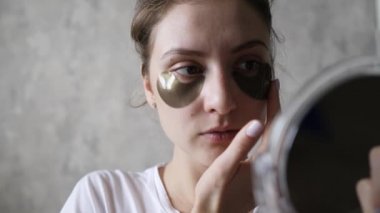 Gözlerinin altındaki deri yüzülüyor. Aynada kendine bakan sağlıklı bir kız tarafından doğal kozmetik ürünler kullanılıyor.