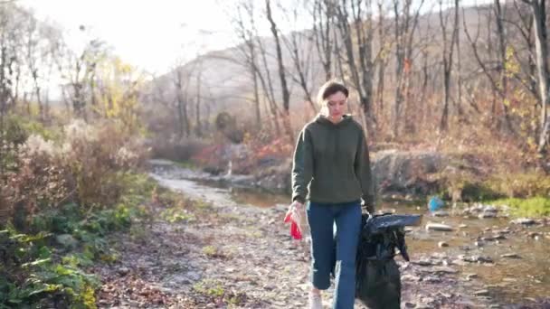 Portret pięknej wolontariuszki na słońcu z plastikową torbą w jesiennym krajobrazie. Zbieranie śmieci i tworzyw sztucznych na zewnątrz — Wideo stockowe