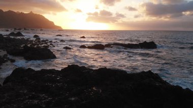 Havadan. Gün batımında plaj. Manzara siyah taşlara ve volkanik kuma açılıyor, altın saat. İnsansız hava aracının görüntüsü. Tenerife, Kanarya Adaları, İspanya