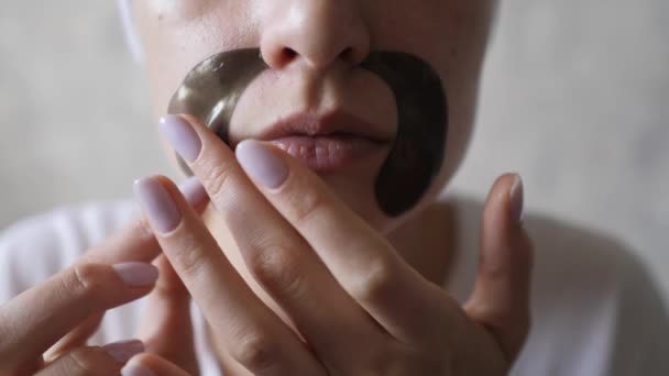 Νεαρή γυναίκα νοιάζεται για το πρόσωπο δέρμα γκρο πλαν. Εφαρμόζεται μπαλώματα γύρω από τα χείλη και χαμόγελα — Αρχείο Βίντεο