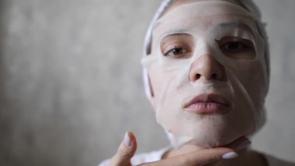 Yüzünde nemlendirici maske ve kafasında havluyla beyaz bir kadının portresi. Sağlıklı yaşam tarzı ve yüz tazeleme — Stok video