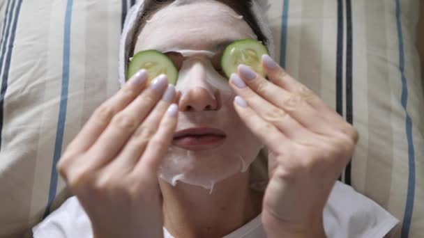 Gyönyörű bőrápolás - egy fiatal nő fehér hidratáló maszkban kerek uborkát tesz a szemére, és a kanapén fekszik
